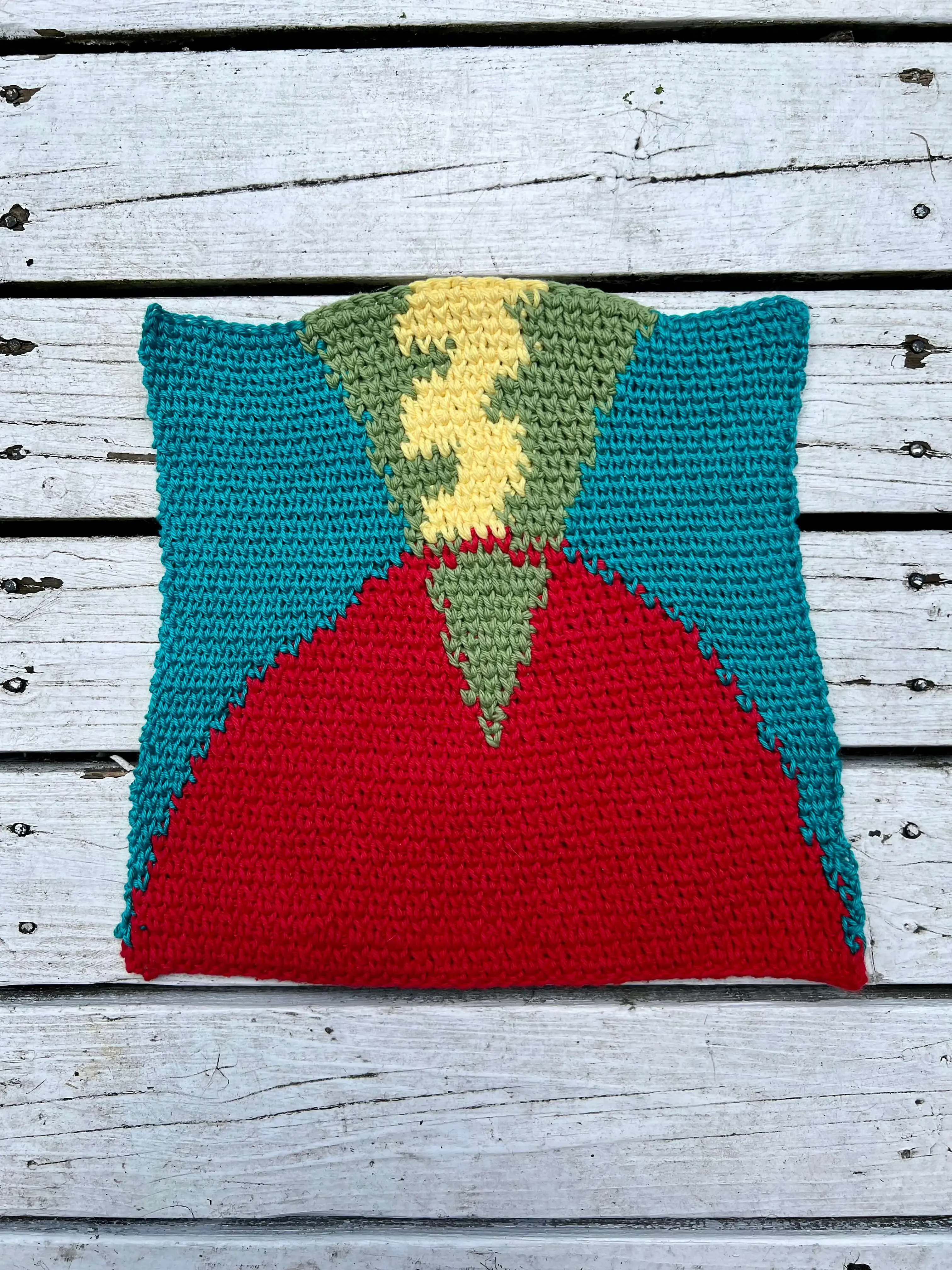 Tapestry of an abstract volcano - A red curved base intersected by a green cone flipped on its point and a yellow squiggle inside that