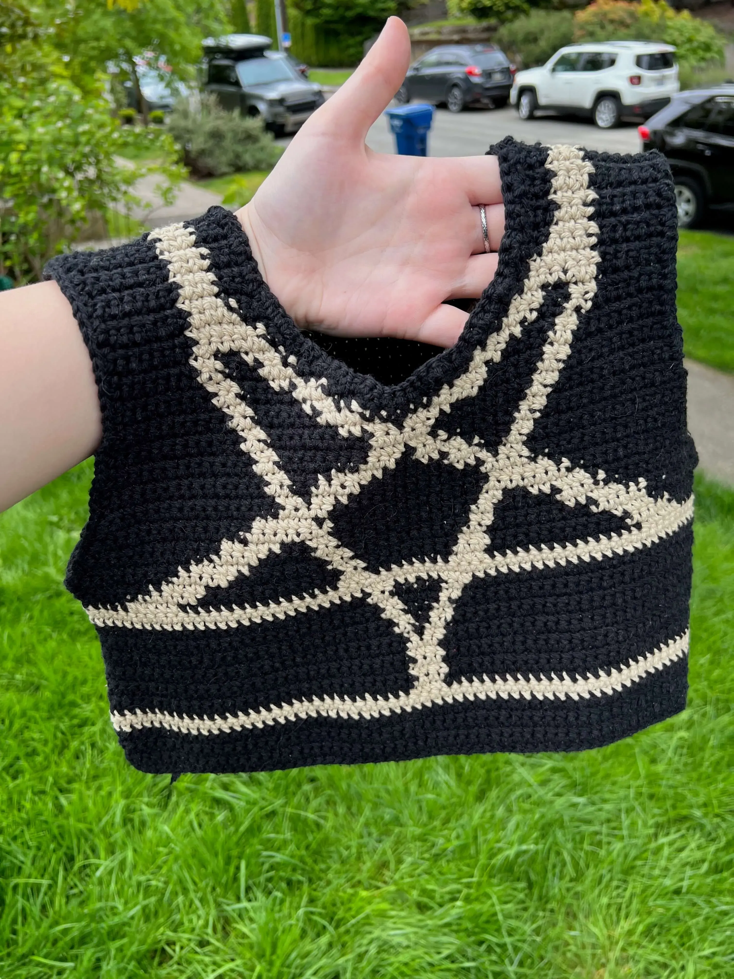 a crochet black binder a tan colorwork design mimicking the shibari inverted star harness hanging from a person's arm