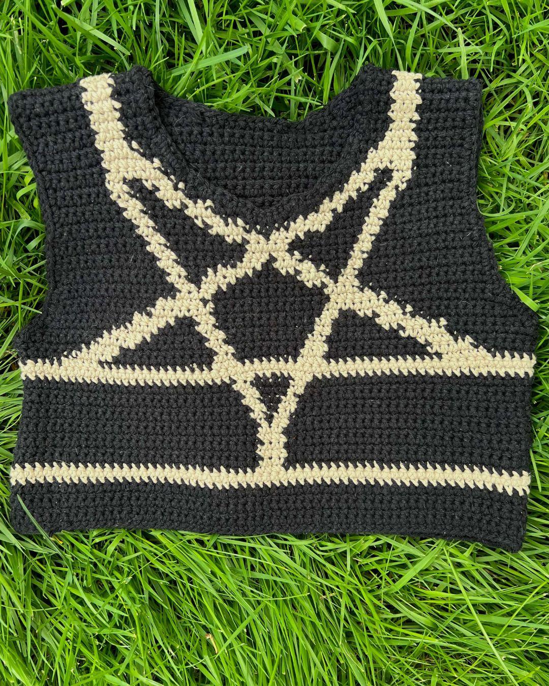 the front of a crochet black binder a tan colorwork design mimicking the shibari inverted star harness