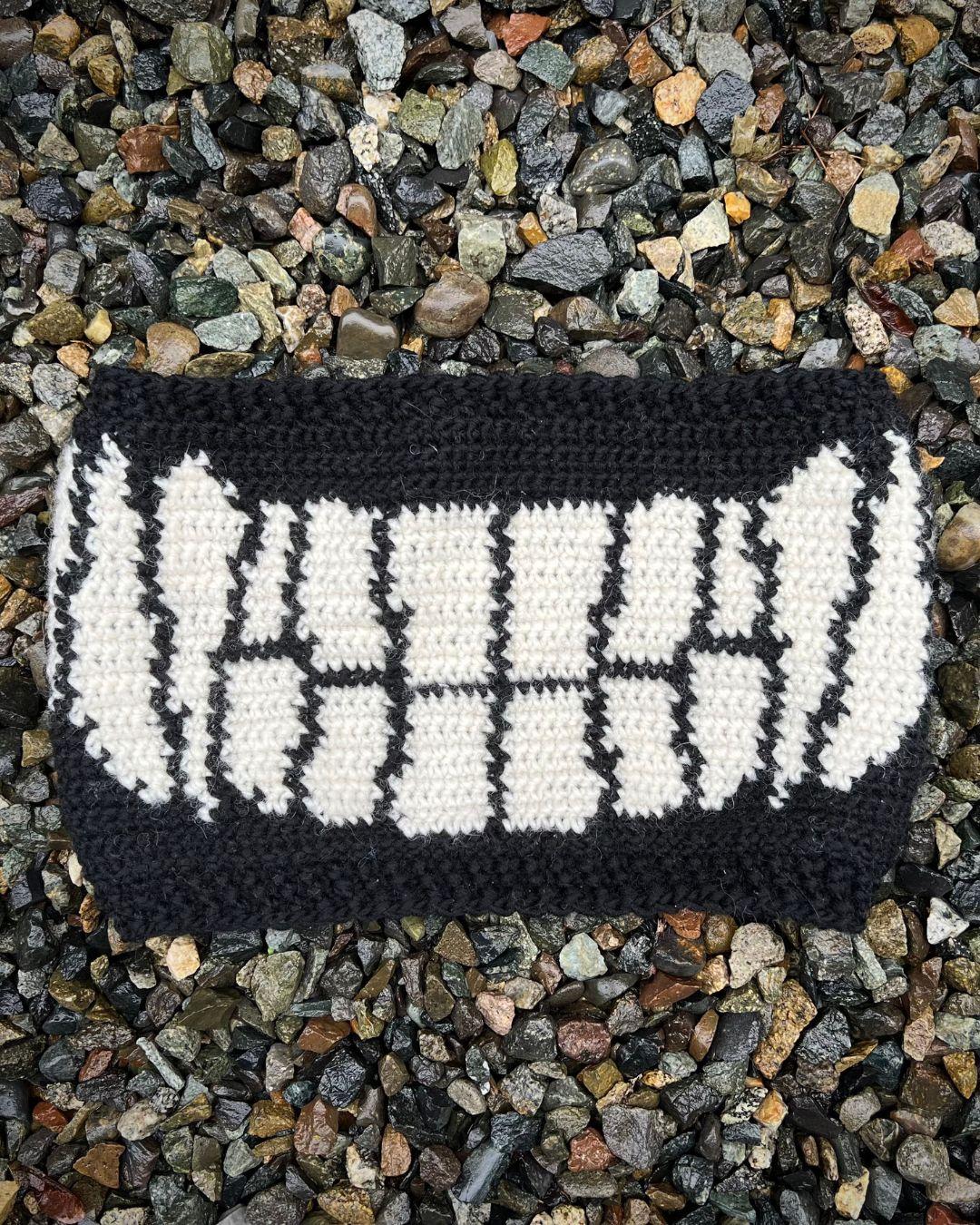 A black cowl with white smiling teeth across the front and 3  sets of fangs on the sides. Laid on top of gravel