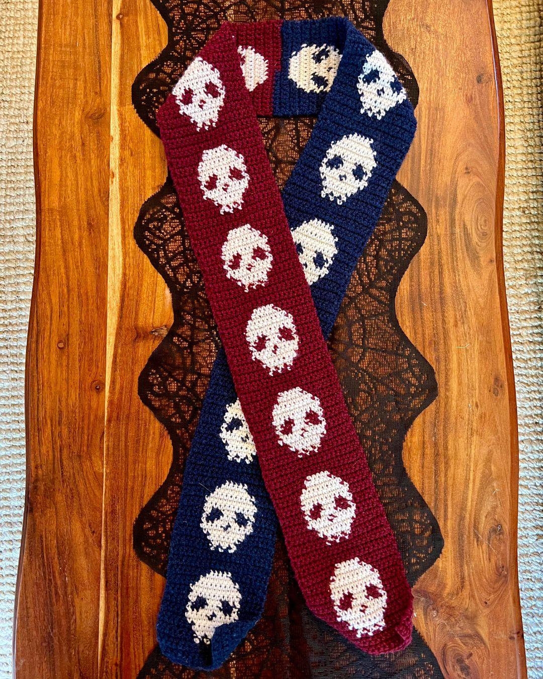 a scarf half blue and half red with repeating skulls for the whole length of the scarf laid on a table in a different arrangement