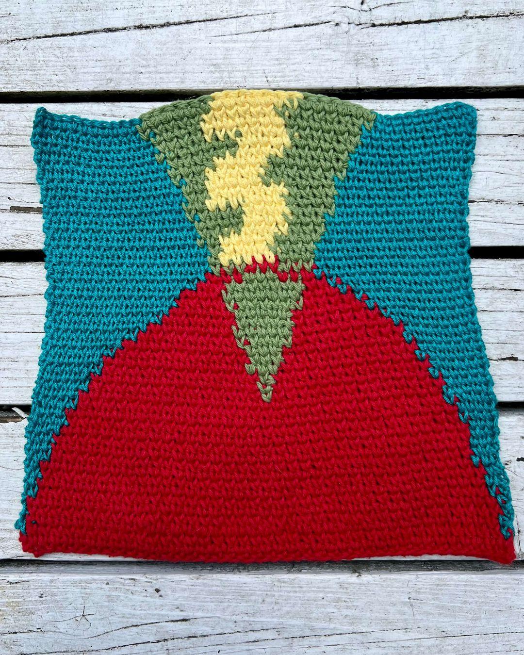 Tapestry of an abstract volcano - A red curved base intersected by a green cone flipped on its point and a yellow squiggle inside that